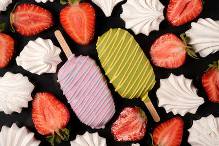Two ice creams with meringue and strawberries on a black background, top view. Bright summer card...