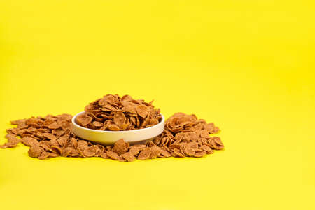 Durum wheat flakes - quick breakfast cereal on a plate on a yellow background, space for textの写真素材