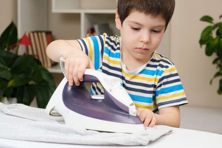 A boy of 4 years learns to hold an iron, iron clothes on an ironing board. Helper, help children to care for the houseの写真素材