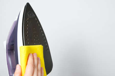 The housewife wipes the dirty surface of the iron with a yellow rag. Cleaning the iron from carbon deposits.の写真素材