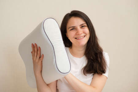 A woman holds an orthopedic pillow made of memory foam and smiles. Choosing the right pillow for healthy sleepの写真素材