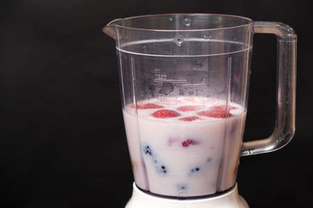 Milkshake in a bowl of a blender of milk, strawberries and blackberries on a black background, a...