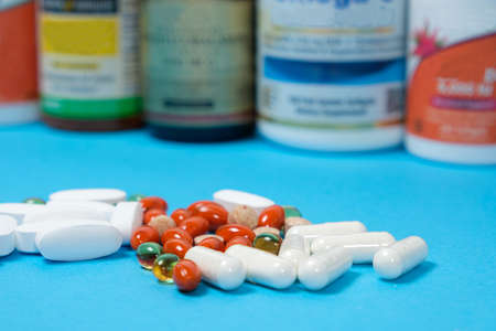 White and orange capsules and pills on a blue background, jars with dietary supplements on the...