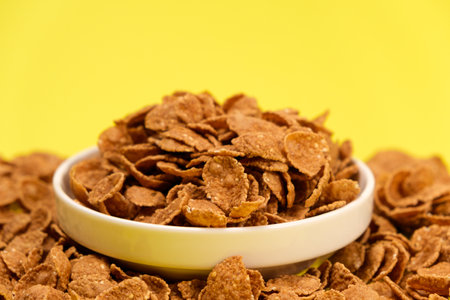 Durum wheat flakes - quick breakfast cereal on a plate on a yellow background, space for text