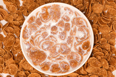 Cereal flakes drenched in milk in a plate, close-up view from above. Healthy delicious dairy...