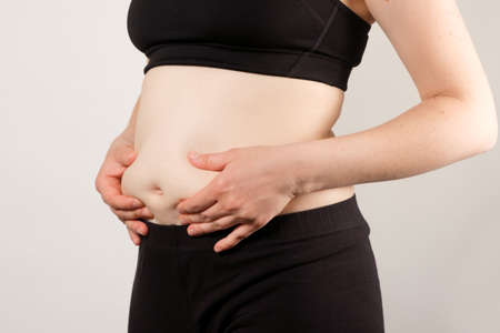 A woman shows an inflated thick belly, the concept of excess weight and weight loss.の写真素材