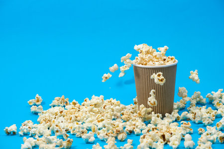 Popcorn is poured into a paper brown glass on a blue background with place for text.の写真素材