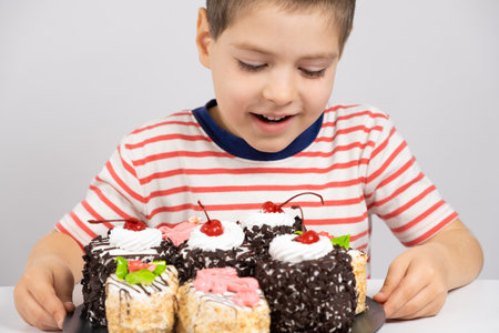 A happy 5 year old boy looks at a delicious cake and smiles on a white backgroundの写真素材