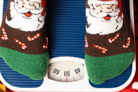 A woman in Christmas socks stands on the scales, weighs herself after gluttony during the holidays.