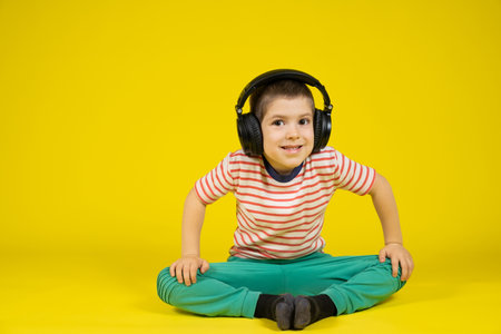 A handsome 5 year old boy in large black headphones sits in the butterfly pose on a yellow backgroundの写真素材
