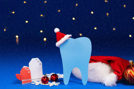 Christmas dentistry - tooth with santa claus hat, mittens on a blue background with snowfall.の写真素材