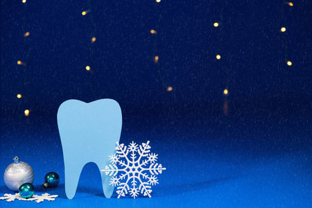 Christmas dentistry - tooth, snowflakes and balls on a blue festive background with bokeh from garlands.の写真素材