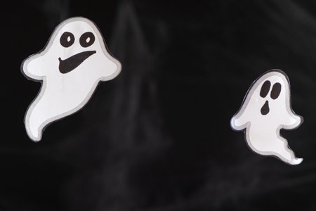 Two merry ghosts with faces fly and smile on a black background with a web. Halloween card, a place for textの写真素材