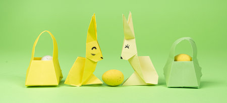 Easter origami - two paper bunnies and an egg, green background. Crafts for the holiday, do it yourselfの写真素材