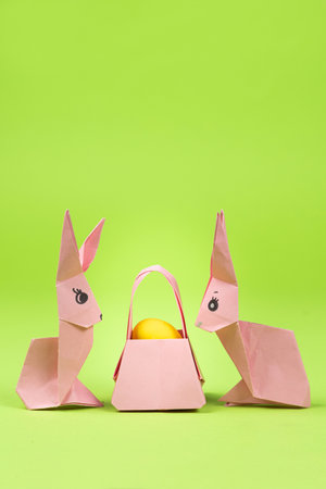Easter origami - two paper bunnies and an egg, green background. Crafts for the holiday, do it yourselfの写真素材