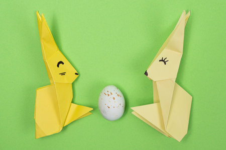 Easter origami - two paper bunnies and an egg, green background. Crafts for the holiday, do it yourselfの写真素材