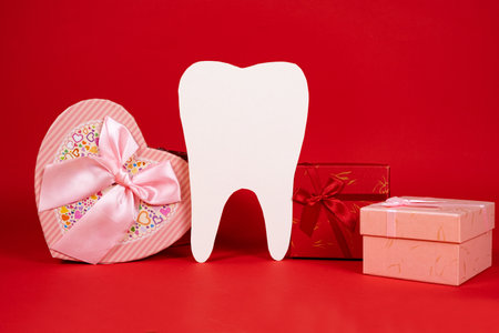 Valentines Day in dentistry - a large white tooth, a heart and boxes of gifts on a red background, a place for textの写真素材