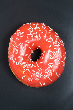 Large doughnut with red glaze and sprinkled on a black backgroundの写真素材