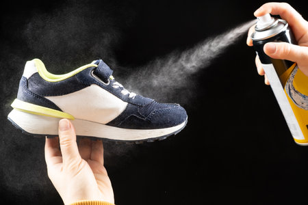 A woman applies a spray from a cylinder with a water-repellent liquid to childrens shoe. Care for shoes, elimination of unpleasant odor.の写真素材