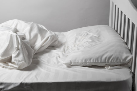 Unmade bed, satin white linen, white bed, pillow and blanketの写真素材