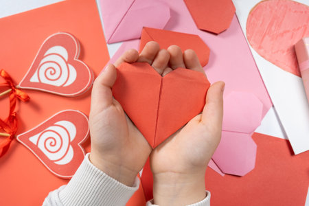 The child creates a hearts out of paper, hands close-up. Origami for Valentines Day.の写真素材