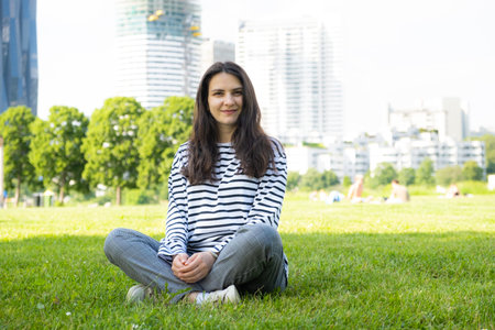 Happy European 30 year old brunette woman sitting on grass in parkの写真素材