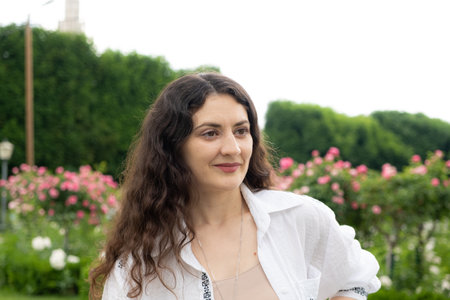 Beautiful successful 35-year-old woman in white shirt walking in the park among roses