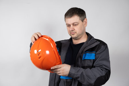 A man in overalls holds a builders helmet in his hands on a white background.の写真素材