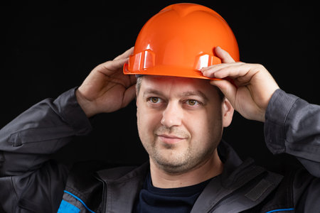 A young man construction worker in a safety helmet and work uniform on a black background.