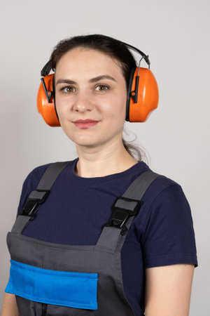 A woman wearing earmuffs and overalls on a white background. Clothing and items for builders, engineersの写真素材
