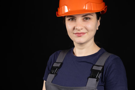 A woman in a protective helmet and overalls on a black background with space for text.の写真素材