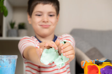 A six-year-old boy plays with slime while sitting at a table at home. A toy for the development of fine motor skills and creativity in childrenの写真素材