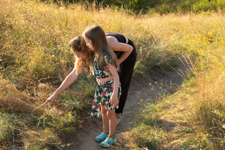 Mother and daughter saw a dangerous animal in the tall grass, a snake or a spider in a summer field.の写真素材
