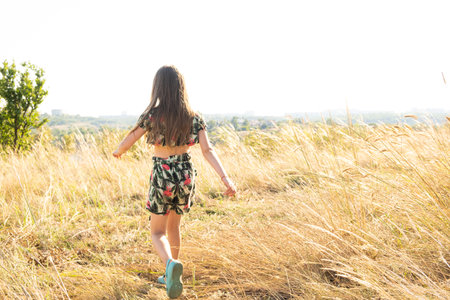 A little 5 or 6 years old girl walks in a summer field of feather grass, a place for text. Carefree happy childhoodの写真素材
