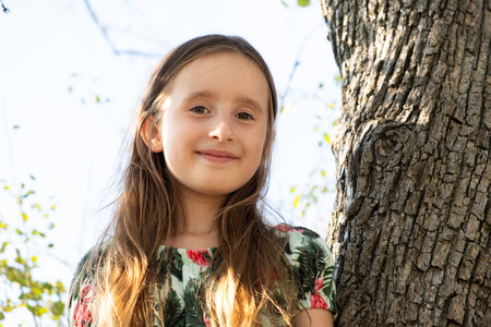 Cute five-year-old girl sitting on a tree in the summer in natureの写真素材