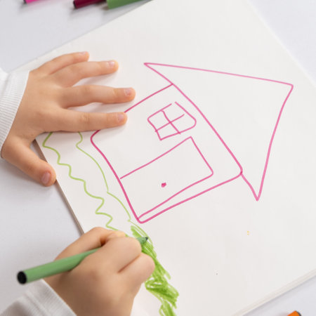 Little child drawing with felt-tip pens a house with grass in a sketchbook.の写真素材