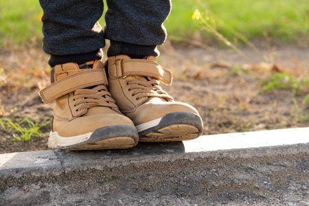 Feet of a little boy in brown nubuck shoes in autumn in a city park. Comfortable waterproof demi-season shoesの写真素材