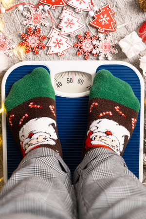 A woman in Christmas socks stands on the scales, weighs herself after gluttony during the holidaysの写真素材