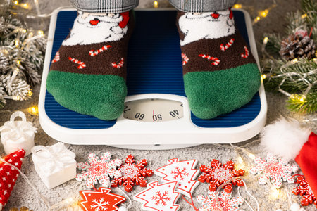 A woman in Christmas socks stands on the scales, weighs herself after gluttony during the holidays
