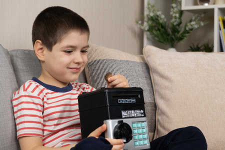 A little boy puts a coin into a safe piggy bank. Financial literacy for children.の写真素材