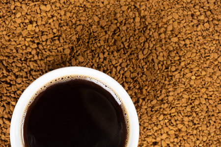 A cup of hot instant coffee on a background of freeze-dried granulesの写真素材