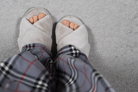 Stylish Modern Fluffy Grey House Slippers on Womens Feet on Carpet, Top View, Place for Textの写真素材