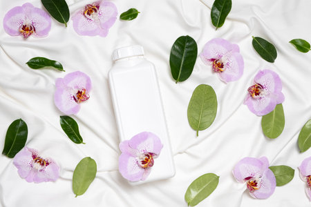 Ecological laundry detergent among orchid flowers on bed linen top view.の写真素材