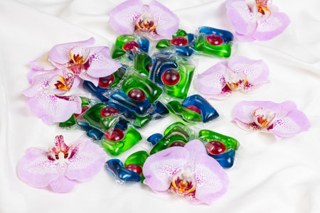 Laundry capsules among orchid flowers on satin fabric.の写真素材