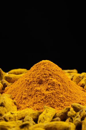 Turmeric powder and dried turmeric root on a black background