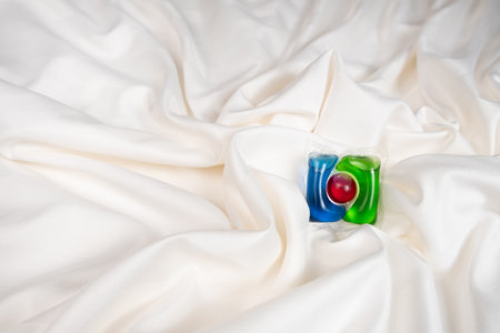 Liquid detergent gel in capsule on fabric close-up, space for text.