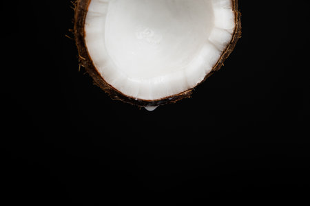 A drop of coconut water dripping from half a coconut on a black background, space for textの写真素材