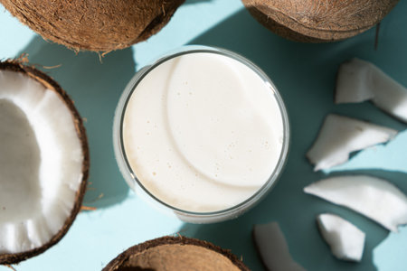 Coconut milk in a glass among coconuts on a blue background top view.