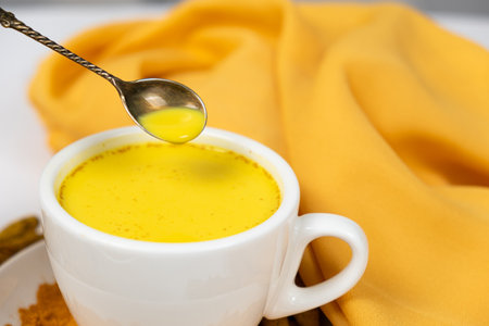 Golden milk with turmeric in a cup, stirring the drink with a spoonの写真素材