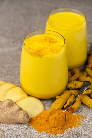 Golden milk, a traditional Ayurvedic drink with turmeric in two glasses on a gray backgroundの写真素材